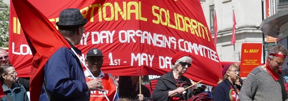 People on a march carrying red banner for May Day